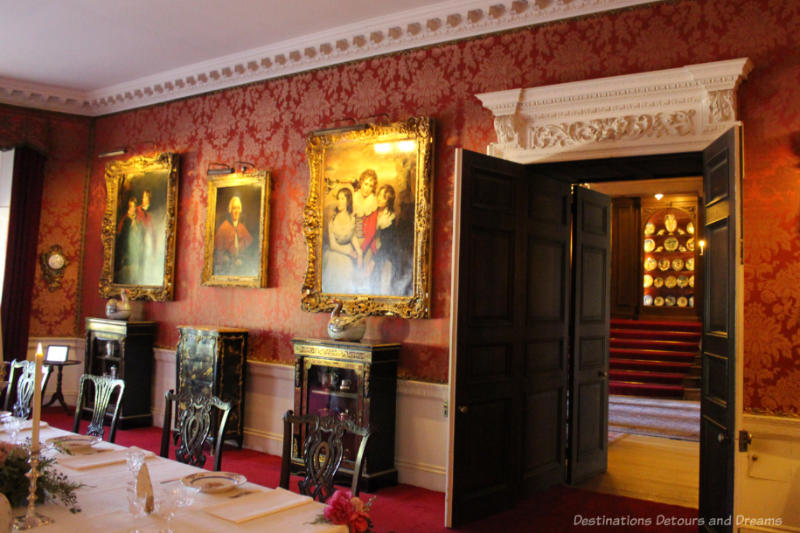 Polesden Lacy dining room with art hanging on red patterned wallpapered walls