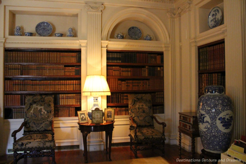 Shelves containing books recessed in white walls with ornate upholstered chairs in front