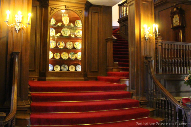Grand red carpeted staircase with dark wood walls at Polesden Lacey