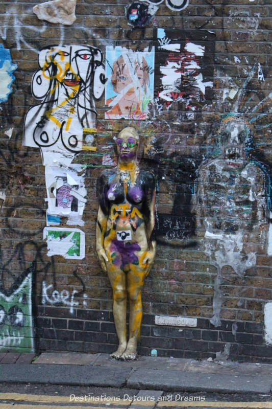 London street art in Brick Lane: work of several artists on Buxton Street building wall includes a three-dimension female body protruding from wall