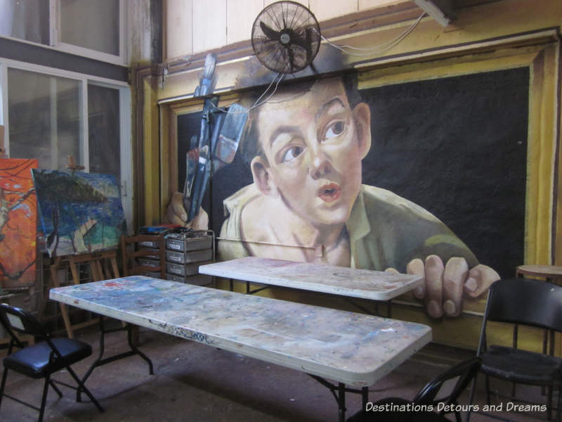 Mural by Adrian Takano of a boy holding paint brushes and coming out of a frame