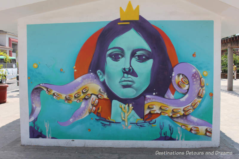 Puerto Vallarta street art: human face with serious expression wearing gold crown and being choked by purple octopus arms