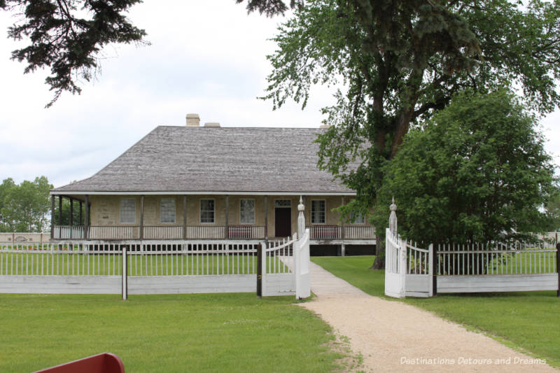 Brick Big House with wraparound veranda inside fenced yard at Lower Fort Garry