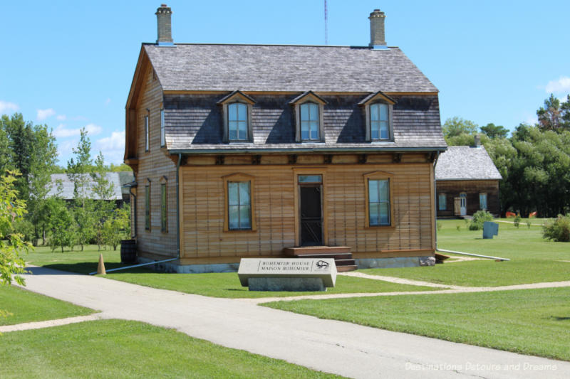 Gambrel-roofed Bohemier house with Turrene log house in background at St. Norbert Provincial Heritage Park, Manitoba