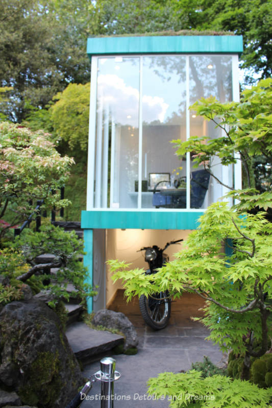 Two storey building with glass-walled tea house on upper level and parking space below in the Green Switch at the 2019 Chelsea Flower Show