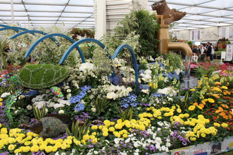 Blue and yellow flowers, blue archway, bronze water pipe, and stream - part of the Floella's Future exhibit at the 2019 Chelsea Flower Show