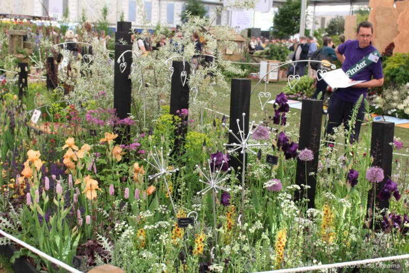 A naturalistic planting of gold and purple flowers with silver garden ornaments at the 2019 Chelsea Flower Show