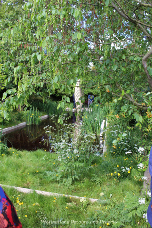 Pond with bronze sculpture in it surrounded by woodland at the Chelsea 2019 Savills and David Harber Show Garden