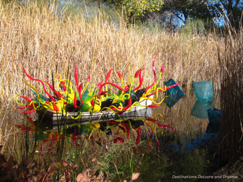 Chihuly sculpture - boat with red and yellow glass pieces and blue crystals in water beside it