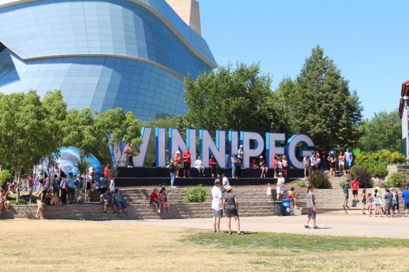 Winnipeg sign with glass panes of the Canadian Museum for Human Rights in the background