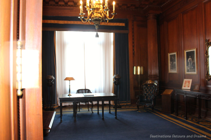 Lieutenant-Governor's Reception Room at the Manitoba Legislative Building has dark wood paneling, blue carpet, and desk as the focal point