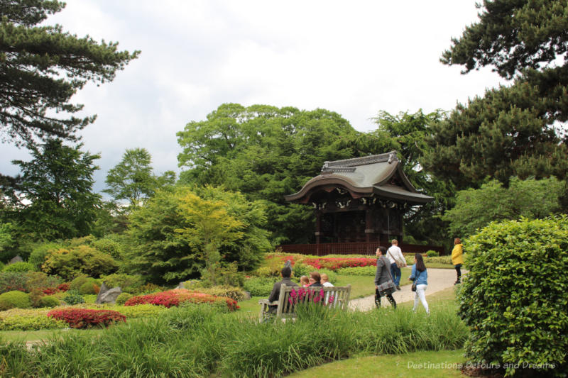 Pathway, bench, shrubs and trees of Japanese landscape at Kew with temple in background