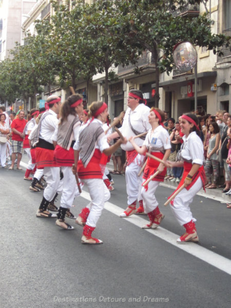 Traditional dancers in white and red with sticks at the Gracia Street Festival parade in Barcelona