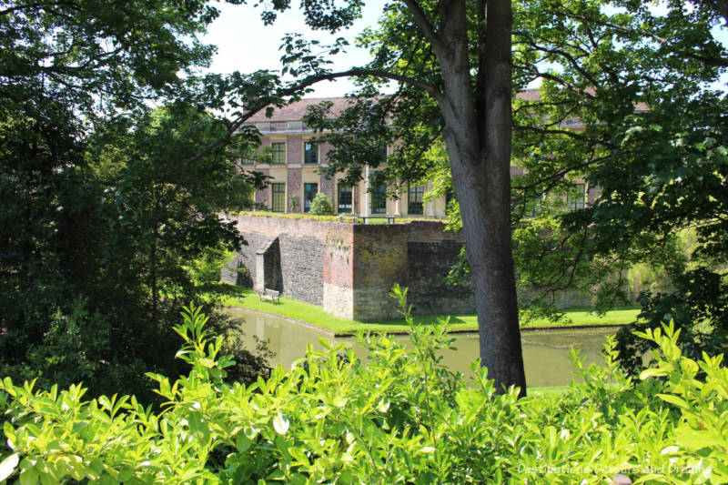 View of brick Eltham Palace through trees and across moat