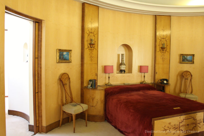 Art deco bedroom with yellow curved wall and decorative wood bedstead and panels beside bed at Eltham Palace