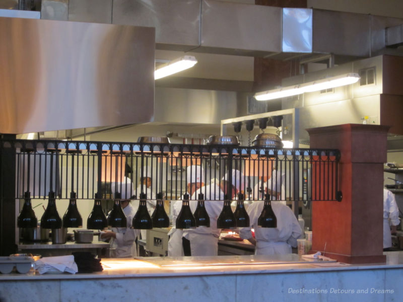 Chefs in restaurant kitchen behind half-wall dividing them from dining area