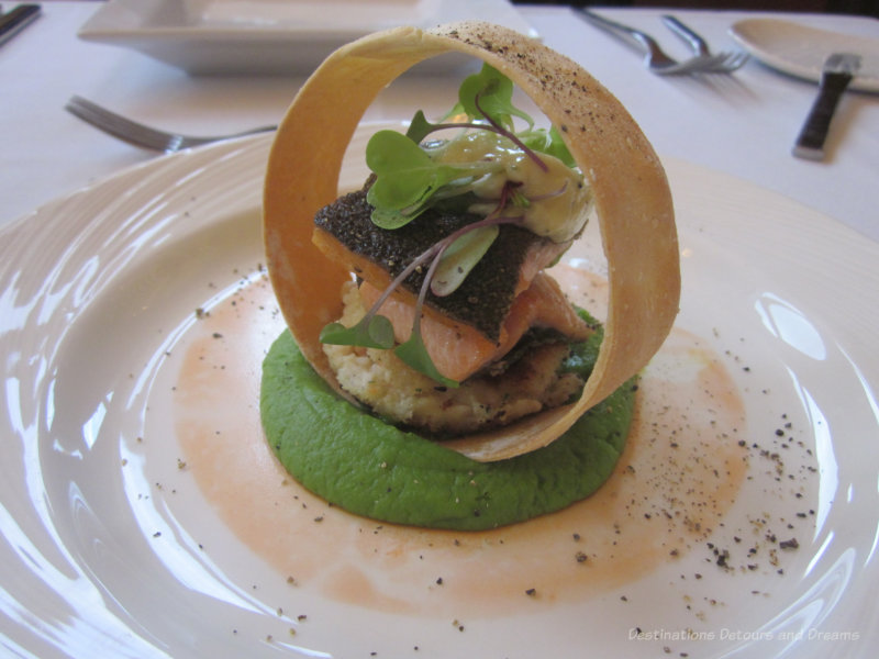 Seared rainbow trout and northern pike cake with horseradish aioli and fresh dill set atop a pea puree, ringed with a crispy potato chip and decorated with carrot paint