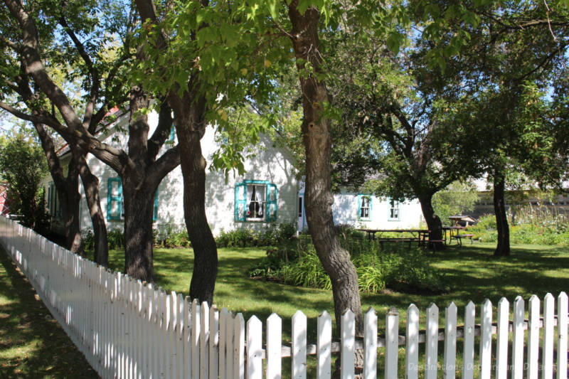 White wooden house with turquoise trim and its white picket-fence trimmed front lawn