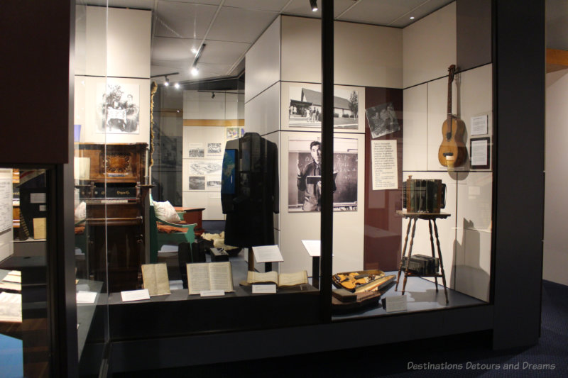 Museum full-size display case with books, musical instruments, photos, and written information