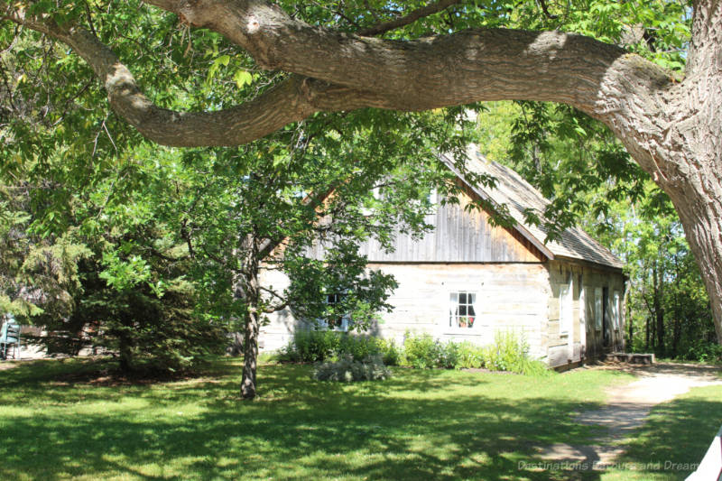 Log house circa 1877 behind a shaded front lawn at Mennonite Heritage Village