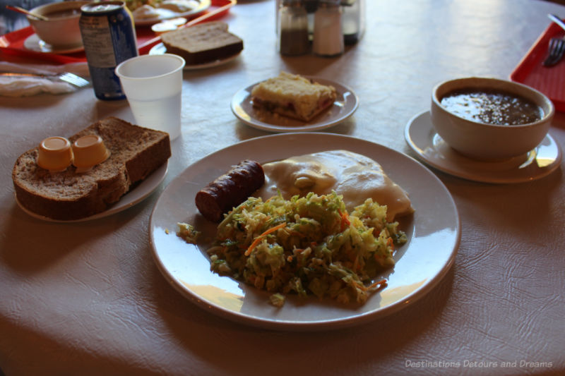 Side plate of bread; main dish of farmer's sausage, vereniki, and coleslaw; bowl of cabbage soup; rhubarb plautz for dessert