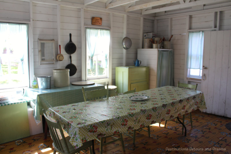 Tables and icebox in a summer kitchen with a wood floor painted with floral designs