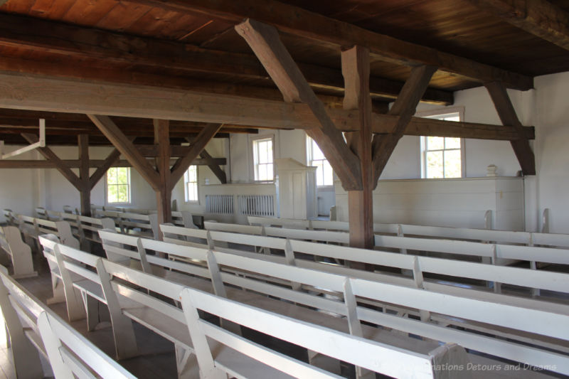 Interior of a plain church building with wood rafters and beams, white walls and white benches