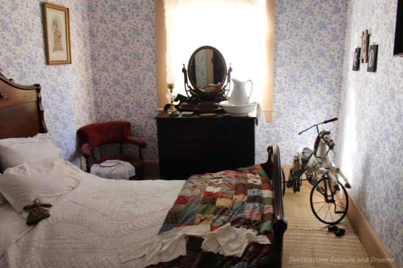 Bedroom from the late 1800s at Ross  Bay Villa with bed, blue patterned wallpaper, and a dark chest