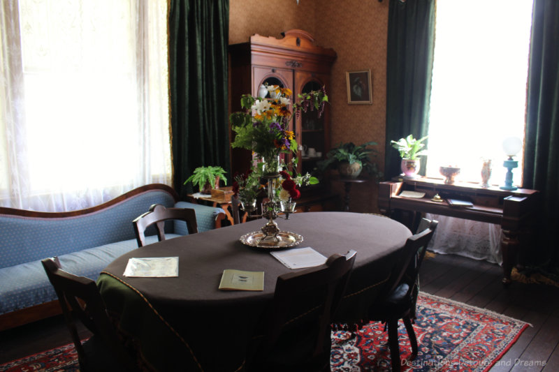 Dining room from the late 1800s with dark oval table and blue settee along the side wall