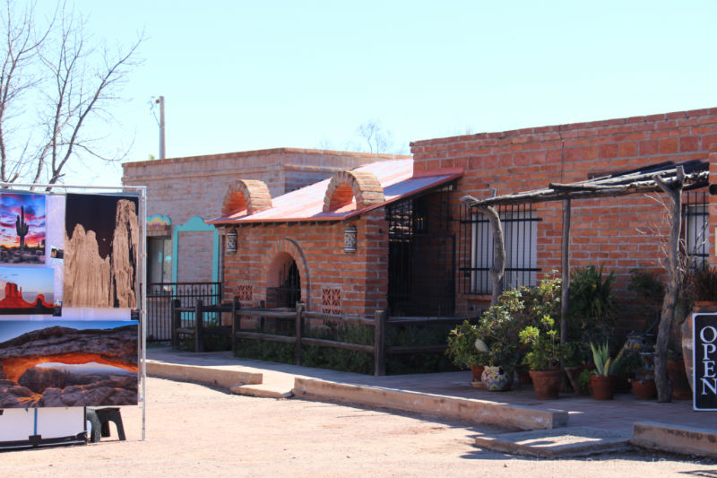 Paintings on display beside a tent at the Tubac Festival of Arts with a brick studio in the background