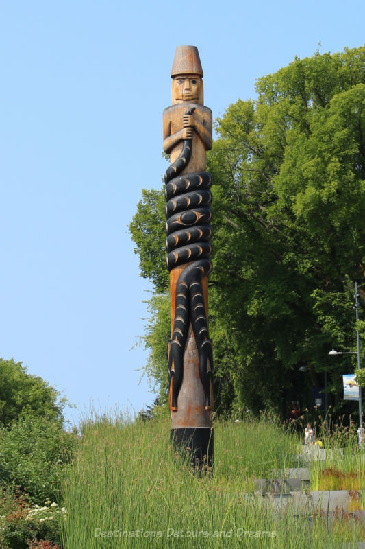 Modern totem pole featuring a human figure at top and a double-headed serpent curling around the pole