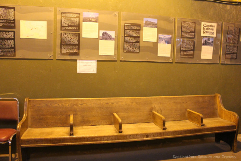 Wooden passenger waiting bench and railway history information on the wall behind it at the Winnipeg Railway Museum