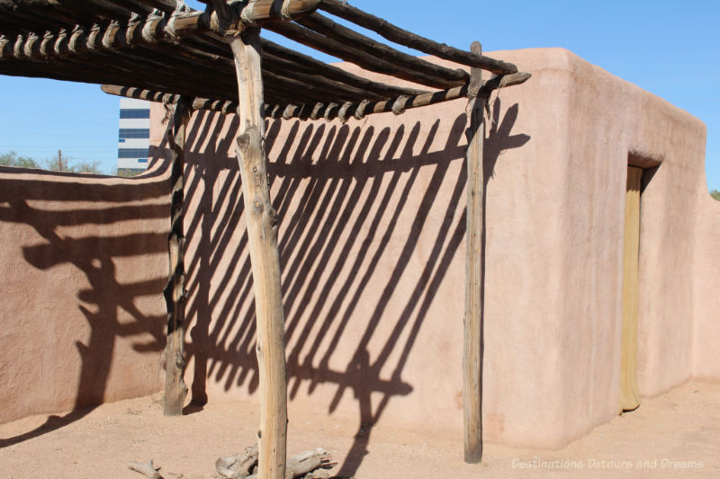 Small adobe building with a ramada shelter beside it