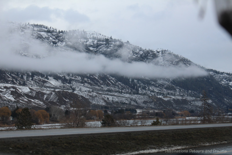 A line of clouds in the middle of partially snow-covered mountains on a winter day