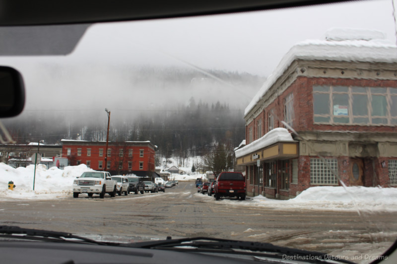 Town street with snow banks along the side and snow piled on rooftops