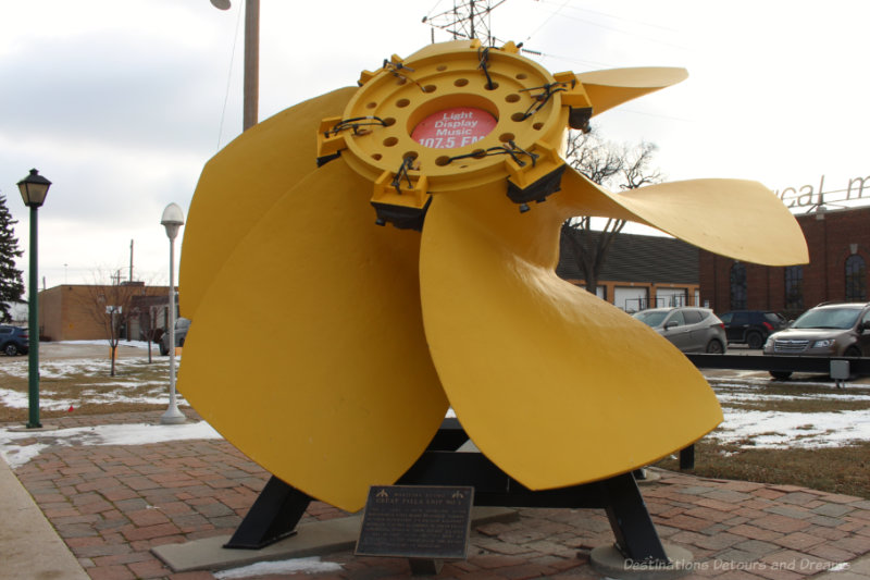A yellow 15-feet and 10-inch diameter fixed blade hydraulic turbine runner from a generating station on display outside the Manitoba Electrical Museum