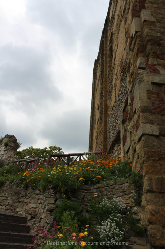 Yellow and orange flowers blooming alongside old stone walls of a medieval castle tower in Guildford