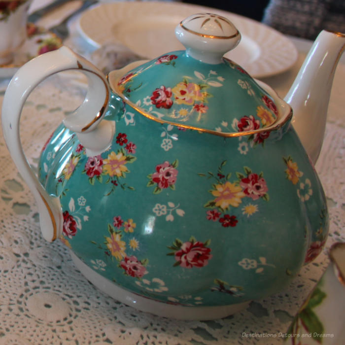 China tea pot with turquoise body decorated with yellow, white, and rose flowers and white handle and spout