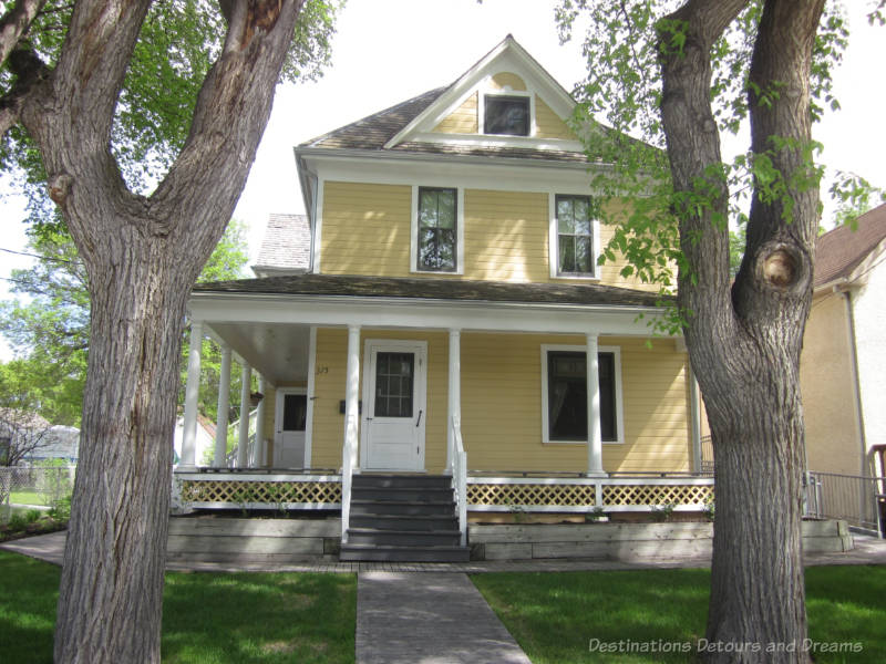 Early 1900s two-story wood house - yellow with white trim - wrap-arpund porch with white columns and lattice railing