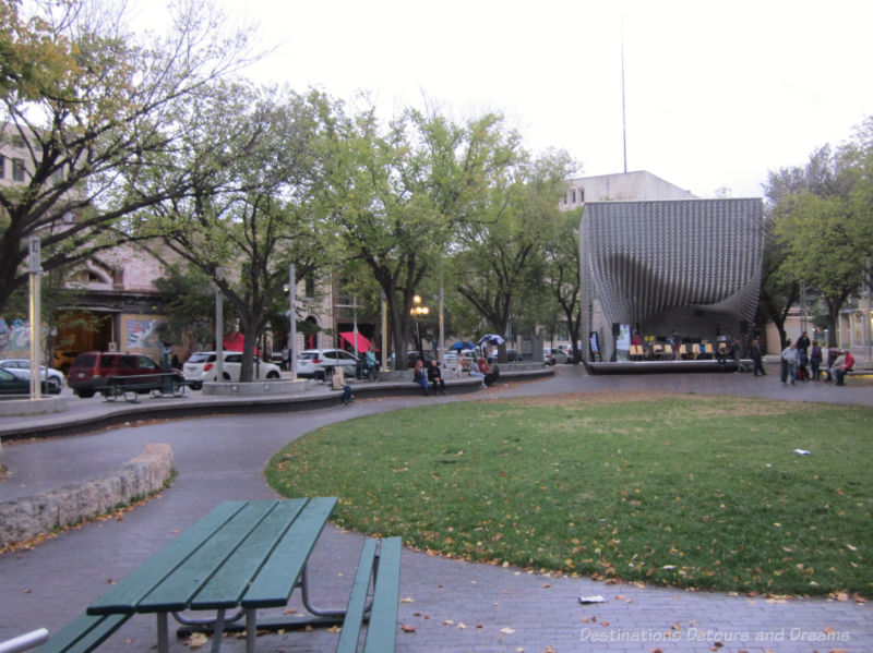 A circle of grass in a city square with a modern stage at one end