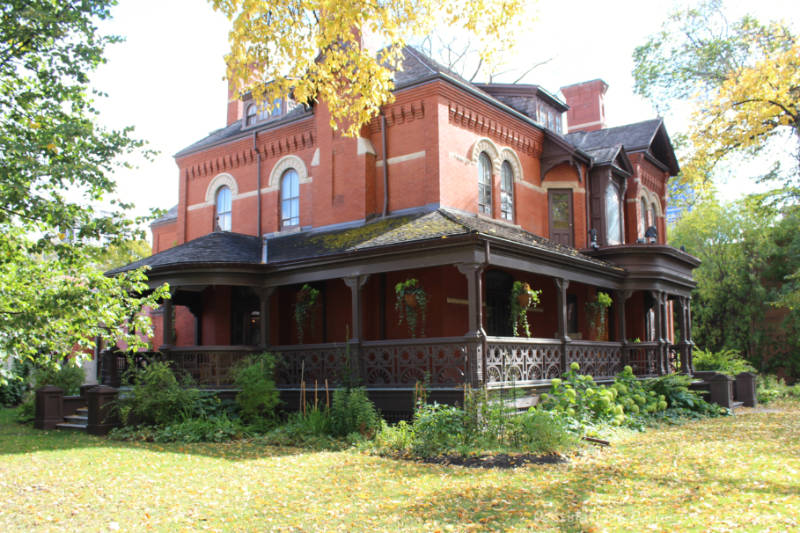 A red brick Victorian mansion with wood wrap-around porch