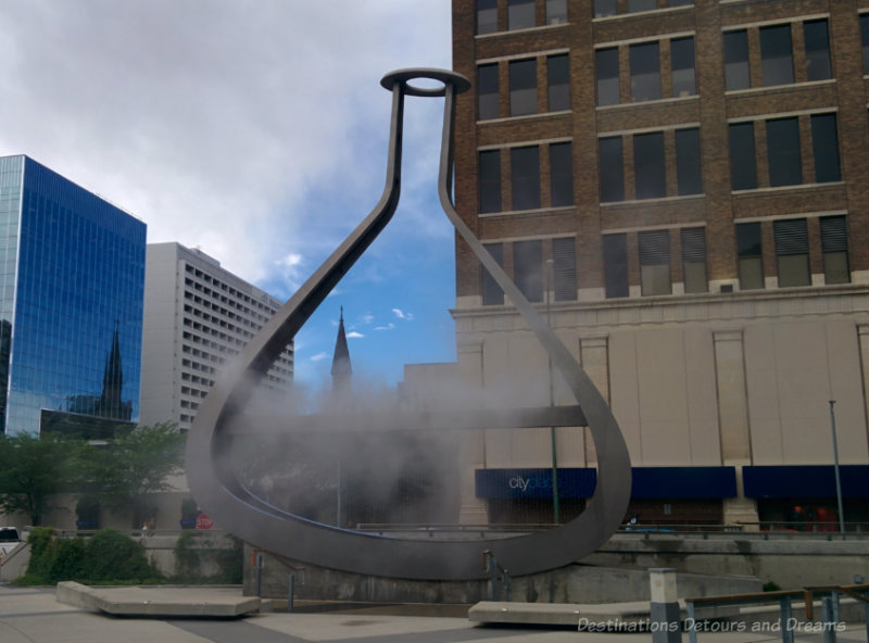 A stainless steel sculpture in the form of a container emanating fog into downtown Winnipeg