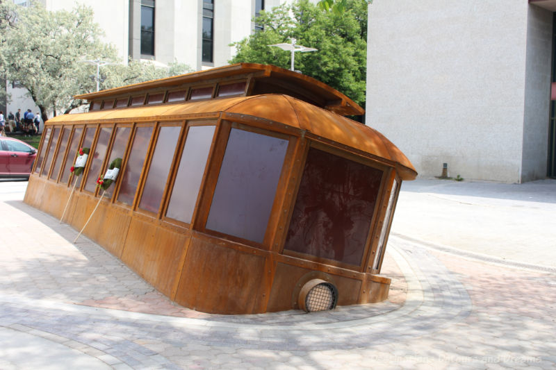 A weathered steel sculpture of a partially submerged, tilted streetcar