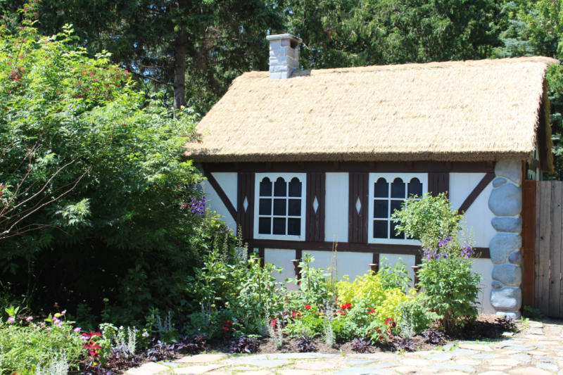 Small cottage with thatched roof, white walls, and brown wood trim in the middle of a garden