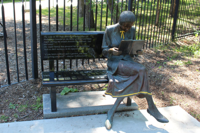 A statue of a woman sitting at one end of a park bench reading a book