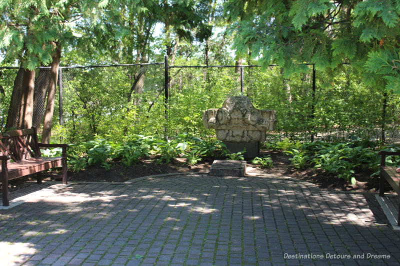 A shaded nook at the end of a stone pathway with benches on either side and a stone monument at the end