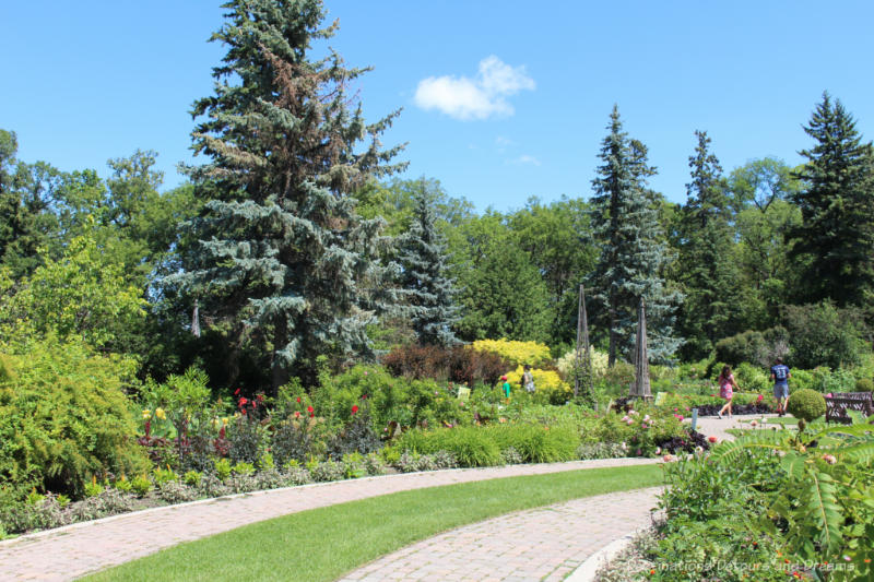 Stone walkways in front of floral plantings against a backdrop of evergreen and deciduous trees