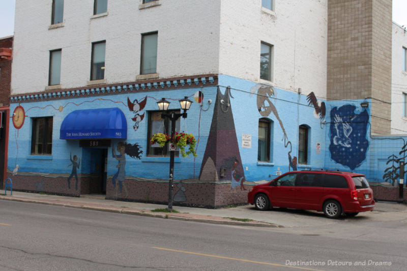 Mural with blue background painted on front and side of a building with Canadian aboriginal symbols