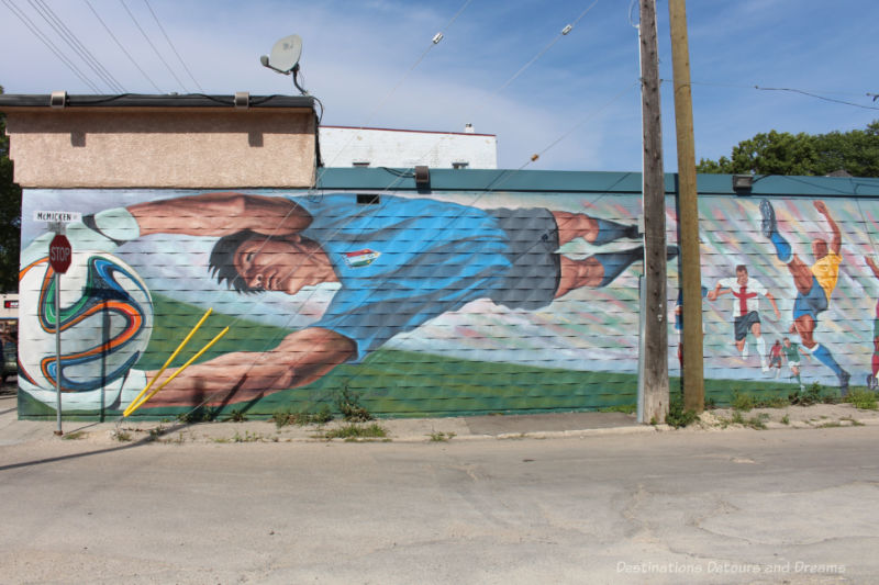 Mural with soccer plays, one of whom is horizontal across the wall reaching for a World Cup ball