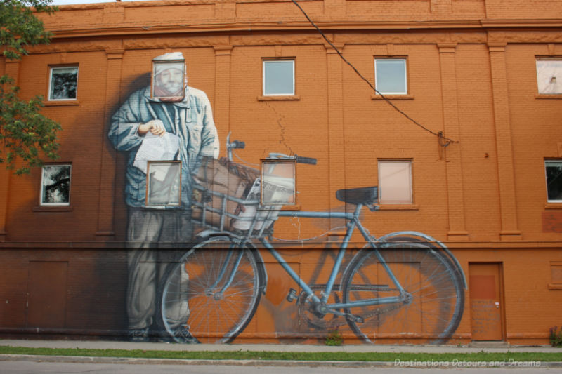 Mural of a large man beside his bicycle on an orange wall